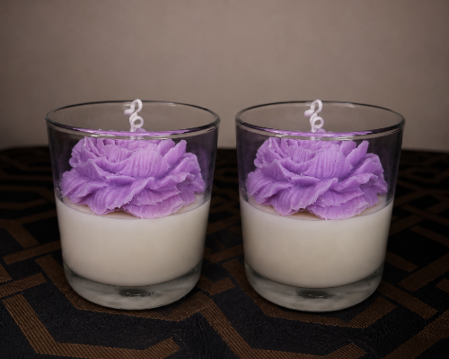Two glass candles with purple floral designs on a dark surface.