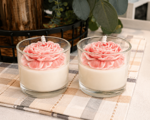 Two glass candles with pink floral designs on a checkered tablecloth.