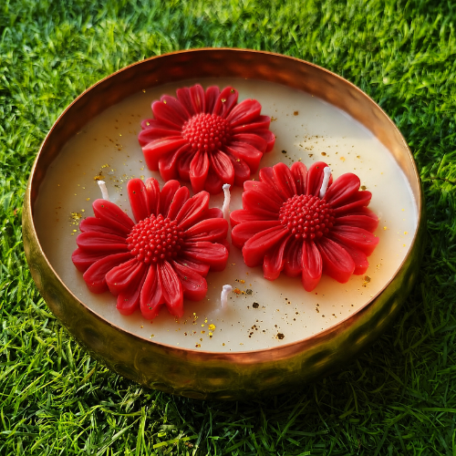 Candle with red flower-shaped wax elements on a grass background