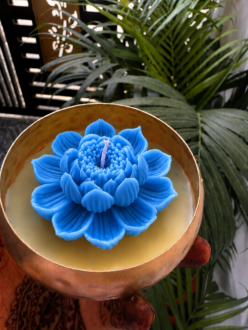 Blue floral candle in a wooden holder with green plants in the background