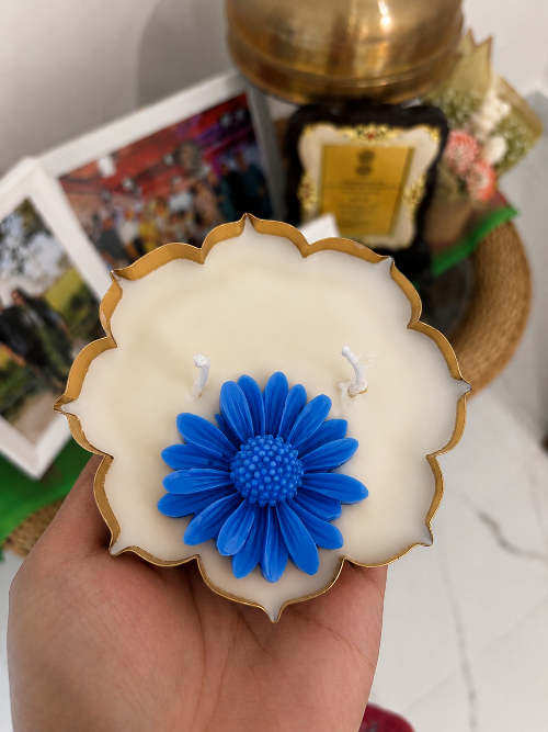Decorative candle with a blue flower design held by a hand, with a blurred background.
