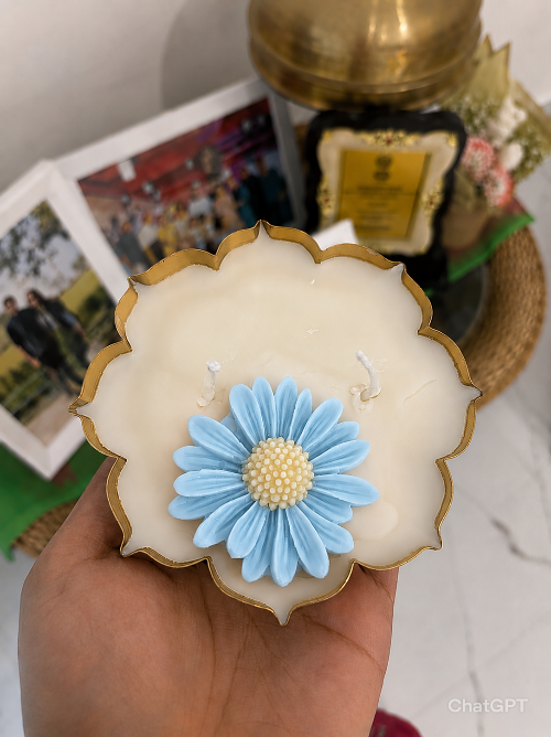 Decorative candle with blue flower design held by a hand, with a blurred background