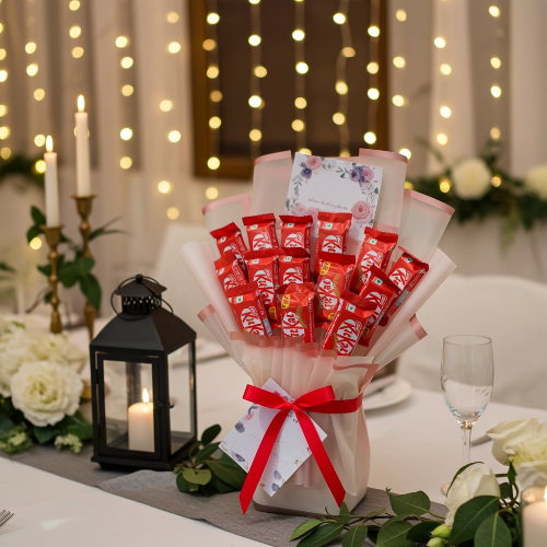 Bouquet of KitKat chocolate bars with a red ribbon on a decorated table with candles and flowers.