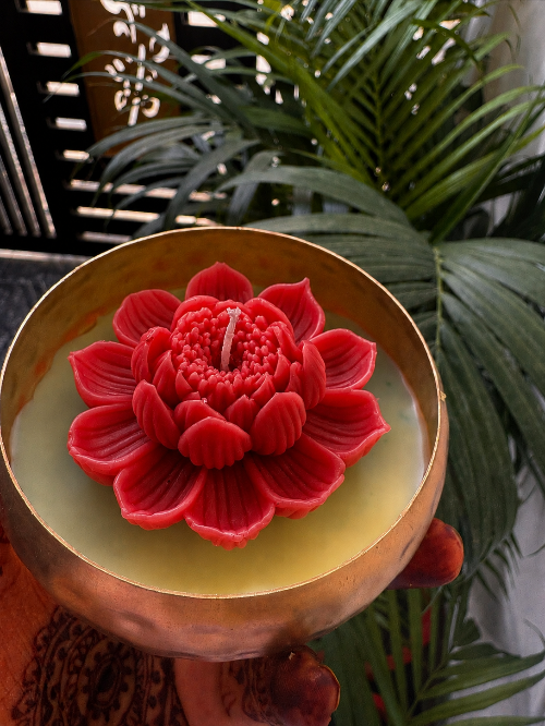 Red flower-shaped candle in a decorative holder with green plants in the background