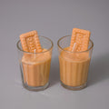 Two glasses filled with a creamy liquid and a biscuit on top against a gray background