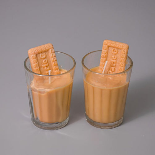 Two glasses filled with a creamy liquid and a biscuit on top against a gray background