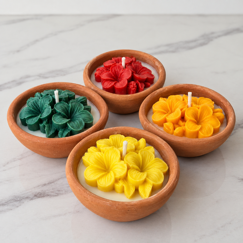 Four small clay candle holders arranged on a light marble surface, each containing a flower-shaped candle in a different color: green, red, yellow, and orange.