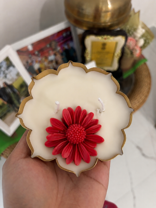 Decorative candle with red flower design held by a hand, with a blurred background