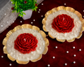 Two red flower-shaped candles on white bases with gold rims on a dark surface.