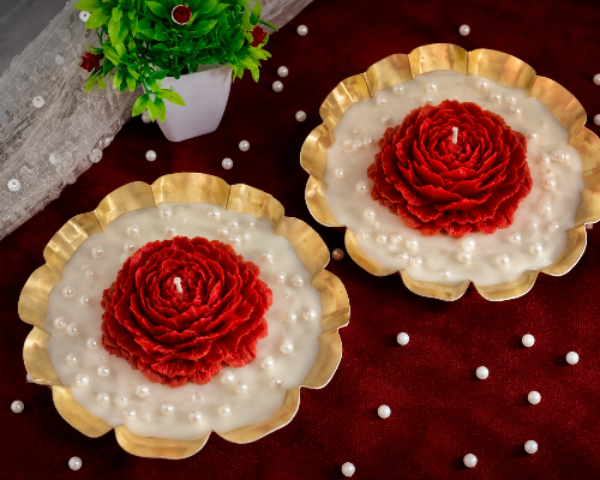 Two red flower-shaped candles on white bases with gold rims on a dark surface.