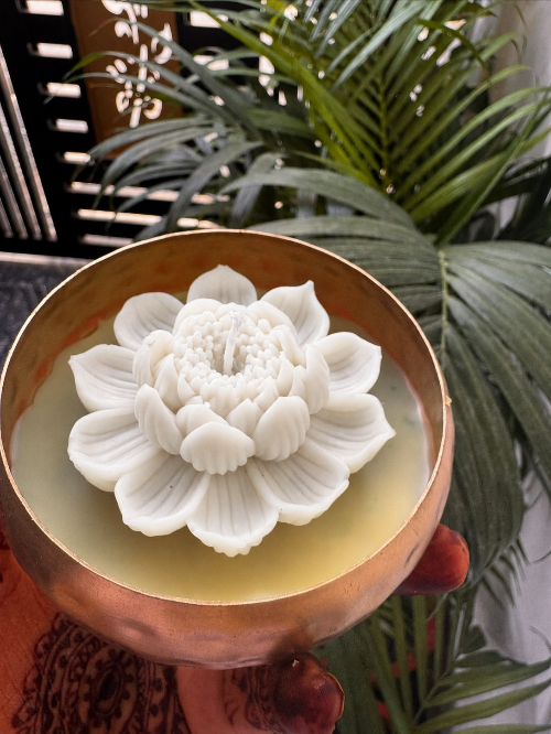 Decorative white flower sculpture in a bronze bowl with green plants in the background