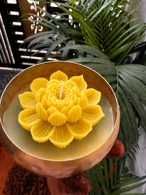 Yellow lotus-shaped candle in a decorative bowl with green plants in the background